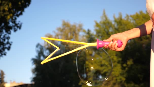 Girl blowing big bubbles in city park against blue sky. Close-up. Slow motion - Footage, Video