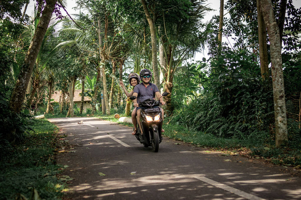 BALI, INDONESIA - DECEMBER 26, 2018: Young couple riding scooter in the rainforest, Bali island. - Foto, immagini