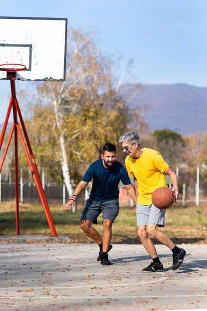 Vader en zoon spelen basketbal in het park - Foto, afbeelding