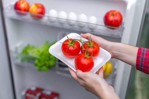 Housewife puts tomatoes in refrigerator. Food storage in the refrigerator. Proper and healthy food. Fresh food and vegetables - Photo, image