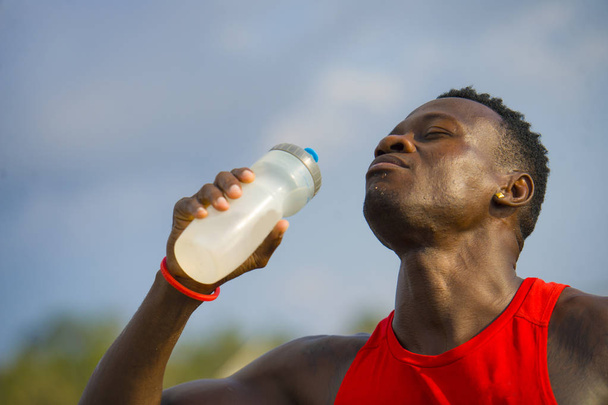 young handsome and attractive black afro American sport man tired and thirsty after running workout holding bottle drinking water or isotonic energy drink recovering in hydration concept - 写真・画像