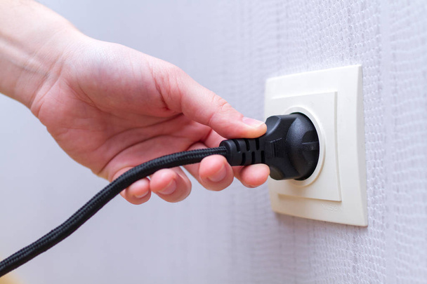 Plugging black power cord cable into wall socket - Фото, зображення