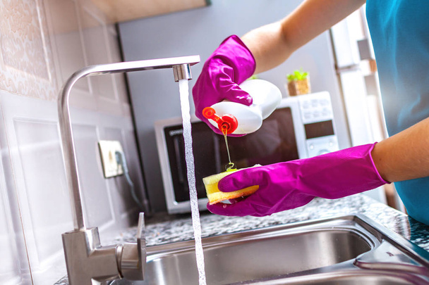 Housewife in rubber colored gloves washing dishes with a yellow sponge in the kitchen at home.  - Foto, Bild