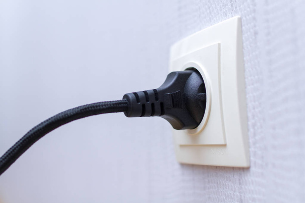 Black power cord cable plugged in wall outlet on wall  - Fotoğraf, Görsel