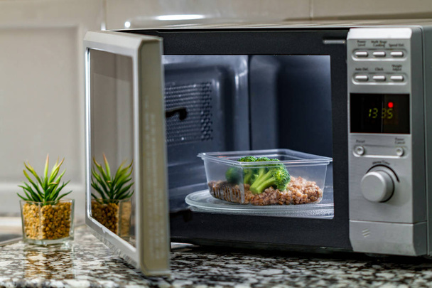 Using the microwave oven to heat food. Heating plastic container with broccoli and buckwheat in the microwave - Photo, Image