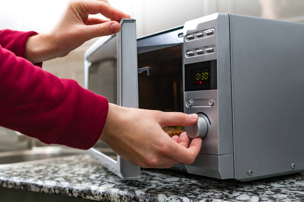 Woman's hand closing the door of the microwave oven and sets the time for heating food - Photo, Image