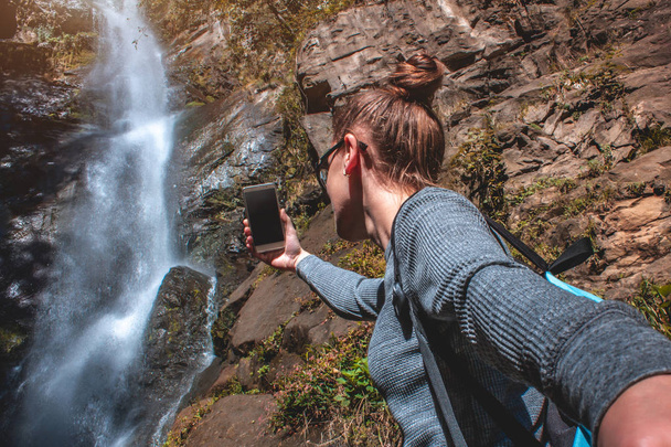 Young girl traveler takes a photo at a waterfall in the mountains. Photos on the background of beautiful landscapes - Fotoğraf, Görsel