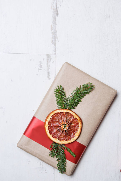 Beautiful hand made rustic Christmas gift box package.Holiday presents wrapped in decorative brown paper decorated with dried orange slice and fir tree branch.Flat lay on wood background - Φωτογραφία, εικόνα
