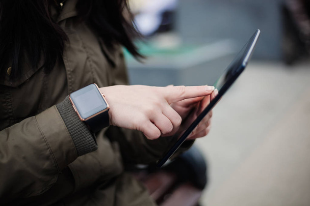 Girl using tablet pc while smart wrist watch is on her hand. This new gadget lets you always stay connected to internet and social media networks from anywhere you want. - Foto, imagen