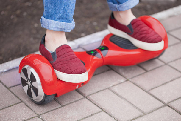 Feet of a gir in marsala shoes riding on modern red electric mini segway or hover board scooter. Trending new transportation technology that is so much fun and easy to ride and produces no air pollution to the atmosphere. Focus on the device - 写真・画像