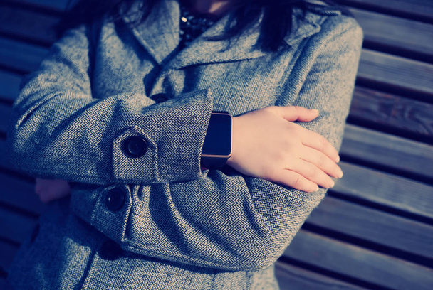 Woman in grey coat weating stylish smart wrist watch. This person is always connected to social media and internet. Modern technology and vintage hipster film toning - Zdjęcie, obraz