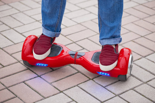 Feet of a girl riding on modern red electric mini segway or hover board scooter. Trending new transportation technology that is so much fun and easy to ride and produces no air pollution to the atmosphere. Close up on model legs and gadget. - 写真・画像