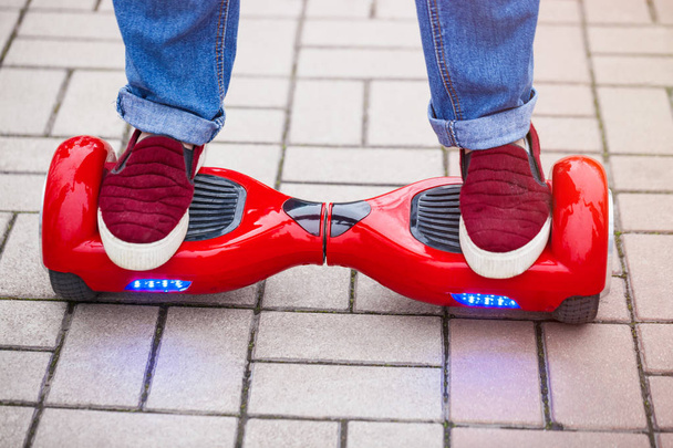 Feet of a woman riding on modern red electric mini segway or hover board scooter. Trending new transportation technology that is so much fun and easy to ride and produces no air pollution to the atmosphere. Close up on model legs and gadget. - Фото, изображение