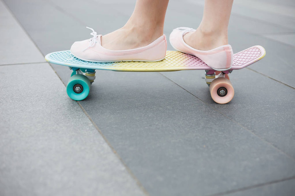 Feet of girl riding modern short cruiser skateboard in pink shoes. Modern and popular skateboarding deck in pink, yellow and turquoise colors - 写真・画像