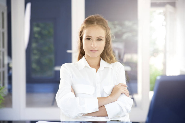 Portrait attractive young businesswoman sitting with arms crossed at office desk behid her laptop and looking at camera. - Foto, Imagen