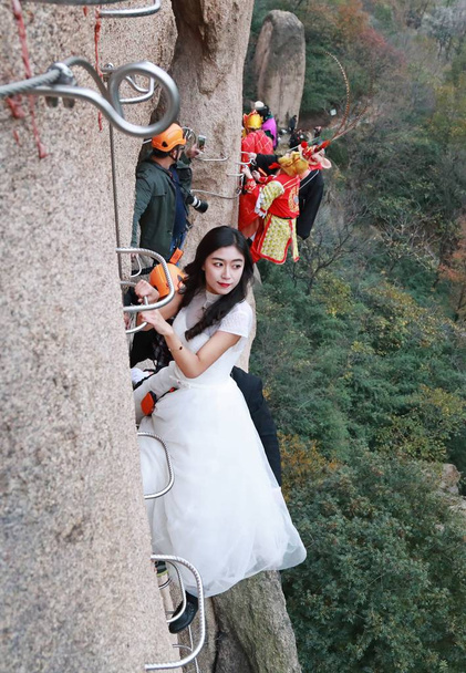 A newlywed Chinese couple poses for wedding photos dangling from a cliff face of the Chaya Mountain scenic spot in Zhumadian city, central China's Henan province, 11 November 2017 - 写真・画像