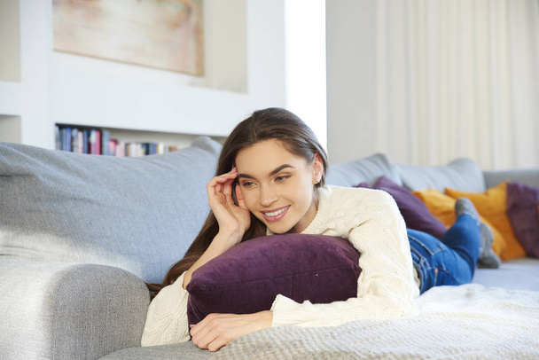 Shot of beautiful young woman lying on sofa and relaxing at home.  - 写真・画像