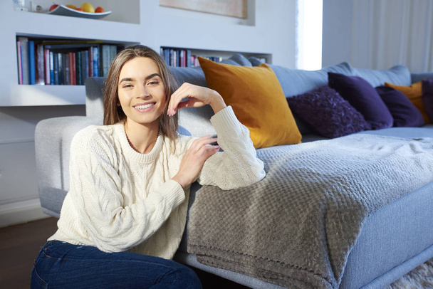 Retrato de una hermosa mujer joven usando suéter mientras se relaja en casa en el sofá. - Foto, Imagen