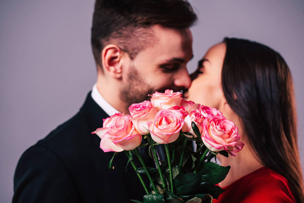 Close up photo of beautiful young romantic couple while they kissing behind the bouquet of roses in hands. St Valentine's day. - Foto, Imagen