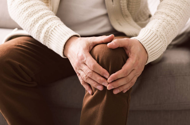 Mature man suffering from knee pain on sofa - Фото, зображення