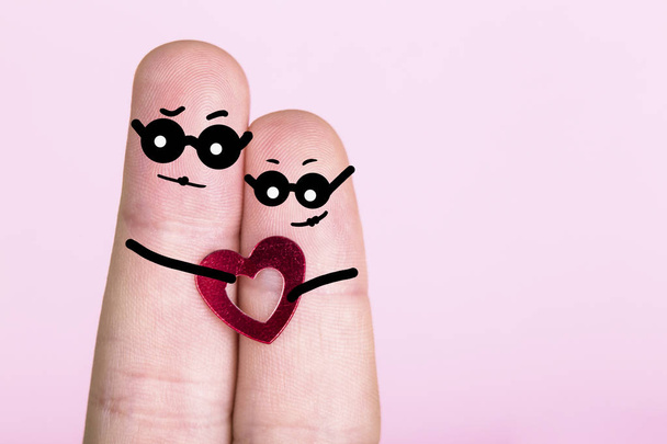dedos con las caras pintadas en gafas sobre un fondo rosa, concepto de una pareja comprometida, en blanco para el Día de San Valentín - Foto, Imagen