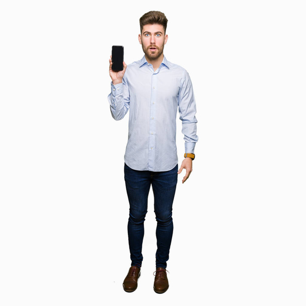 Genç yakışıklı adam iş gösteren smartphone ekran şok sürpriz yüzü, korkuyor ve korku ifadesi ile heyecanlı olan korkmuş - Fotoğraf, Görsel