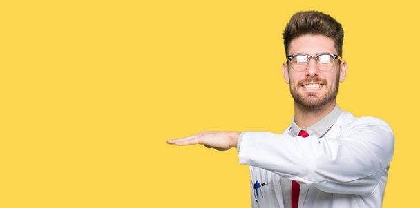Young handsome scientist man wearing glasses gesturing with hands showing big and large size sign, measure symbol. Smiling looking at the camera. Measuring concept. - Fotó, kép