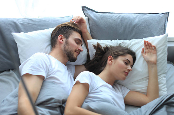 Beautiful young loving couple sleep and making selfie with stick in the bed. - Фото, изображение