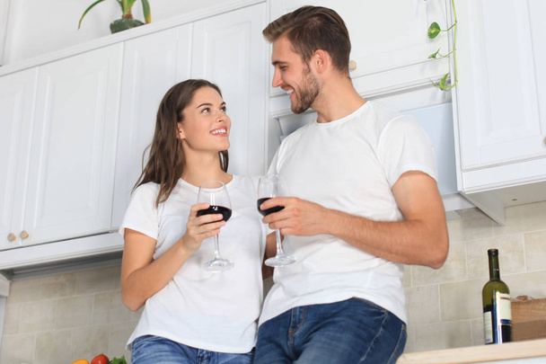 Beautiful young couple is drinking wine and smiling while cooking in kitchen at home. - Foto, afbeelding