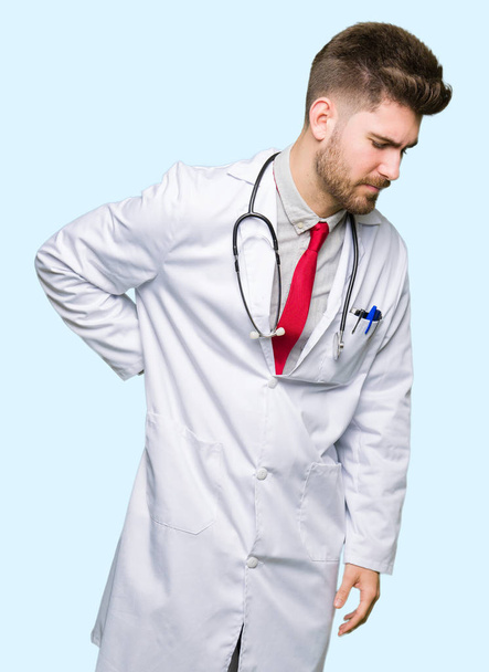 Jonge knappe dokter man met medische jas lijden van rugpijn, aanraken terug met hand, spierpijn - Foto, afbeelding