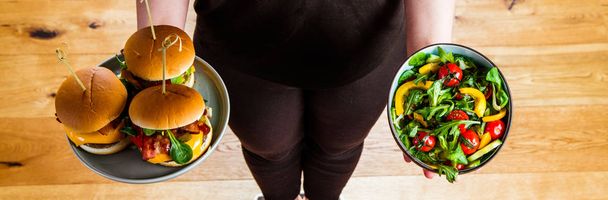 Jeune femme saine regardant des assiettes saines et malsaines de la nourriture, en essayant de faire le bon choix
  - Photo, image