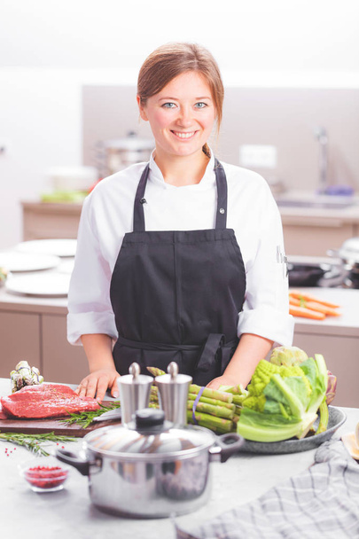 Smiling female kitchener in uniform is standing in the kitchen at the restaurant. - Foto, imagen