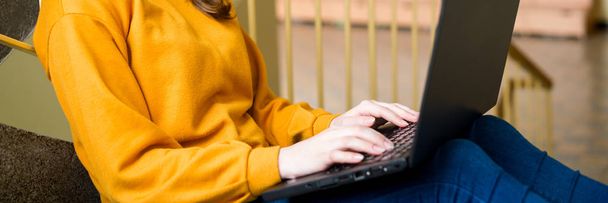 Young female college student sitting on stairs at school, writing essay on her laptop. Education concept. - Photo, image