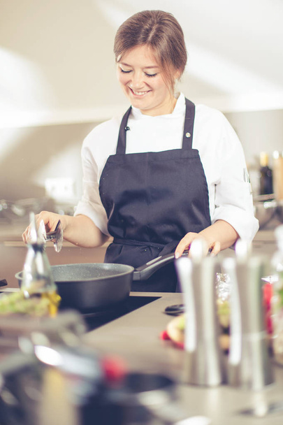 Une cuisinière souriante en uniforme se tient debout dans la cuisine du restaurant. - Photo, image