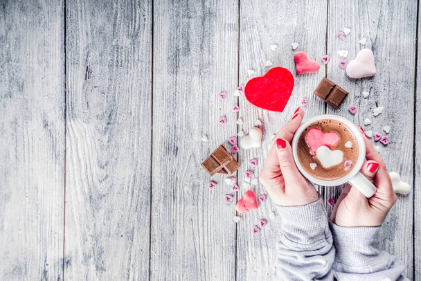 Meisje handen houd warme chocolade met marshmallow harten, rood roze witte kleur met chocoladestukjes, suiker hagelslag, oude houten achtergrond kopie ruimte bovenaanzicht, handen in pictute flatlay - Foto, afbeelding