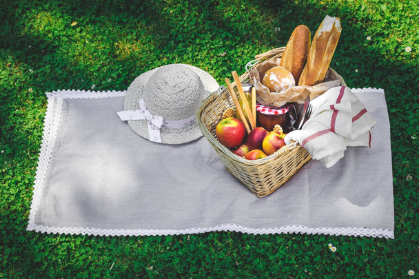 Hat, straw basket with food and drinks on beige plaid . - Photo, image