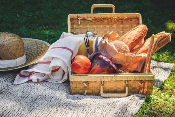 Picnic basket filled with fruit , bread and jar with apricot jam on beige plaid. - Photo, Image
