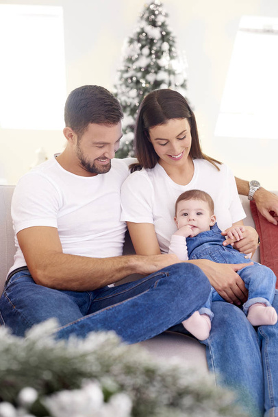 Shot of happy young family sitting on sofa with their baby girl and enjoy relaxing at home. - Foto, Bild