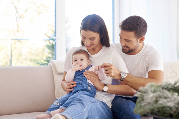 Shot of happy young family sitting on sofa with their baby girl and enjoy relaxing at home.  - Foto, Imagem