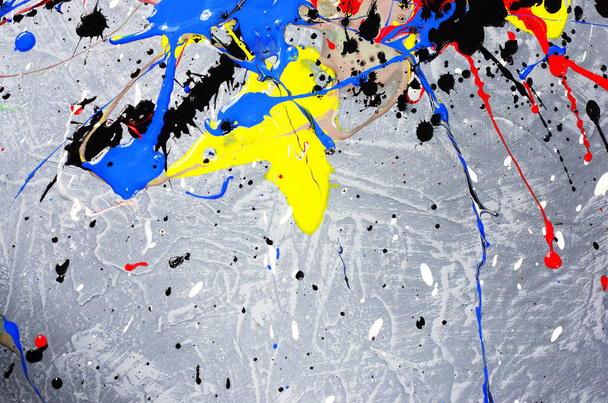 una mancha de pintura derramada blanca y negra y amarilla y verde y roja y azul sobre una superficie texturizada de hormigón
. - Foto, imagen