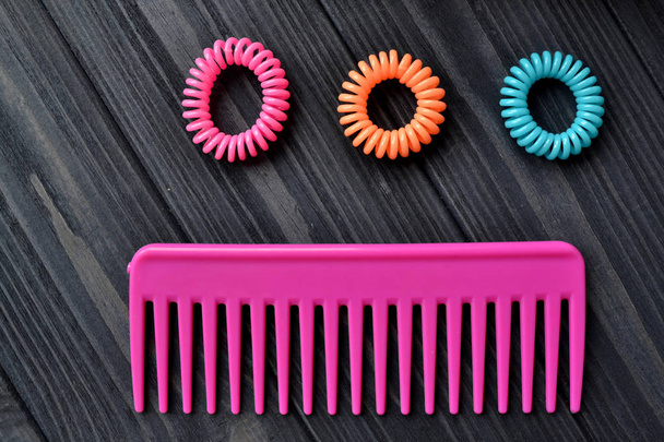 Hair care instruments. Beauty salon. Hair care tools on the dark blue wooden background. Hair Dryer, curling iron, comb and bright spiral scrunchies. - Foto, Bild