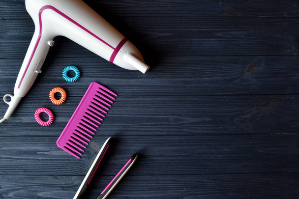 Hair care instruments. Beauty salon. Hair care tools on the dark blue wooden background. Hair Dryer, curling iron, comb and bright spiral scrunchies. - Photo, Image