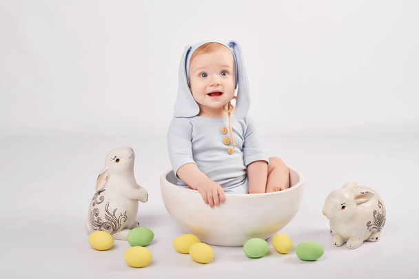 Toddler boy in an Easter bunny costume on a light background with Easter eggs - Photo, Image