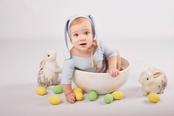 Niño pequeño en un traje de conejo de Pascua sobre un fondo claro con huevos de Pascua
 - Foto, imagen
