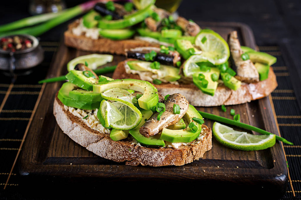 Sandwiches with sprats, avocado and cream cheese on wooden board - Photo, Image
