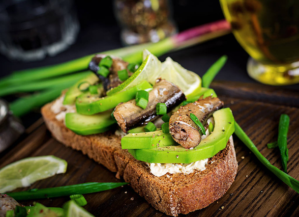 Sandwiches mit Sprotten, Avocado und Frischkäse auf Holzbrett - Foto, Bild