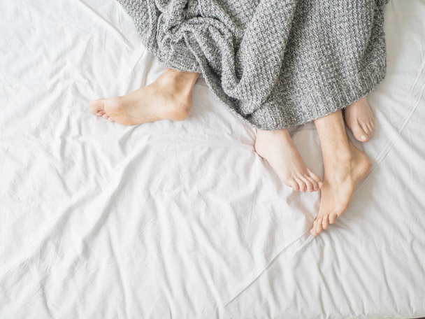 Füße von zwei Paaren, die auf einem Bett unter einer Decke schlafen. Liebe und Beziehungskonzept - Foto, Bild