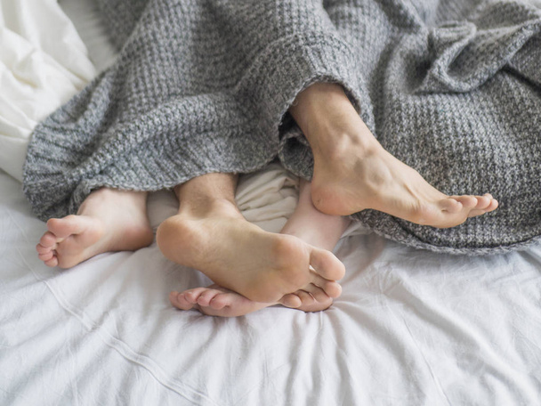 Pies de dos parejas durmiendo en la cama debajo de la manta. Concepto de amor y relación
 - Foto, Imagen