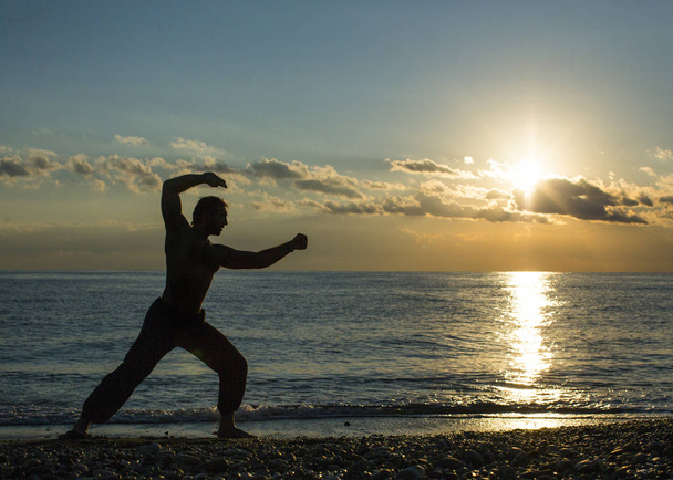 Одинокий мужчина занимается боевыми искусствами на пляже во время заката. Ушу
. - Фото, изображение