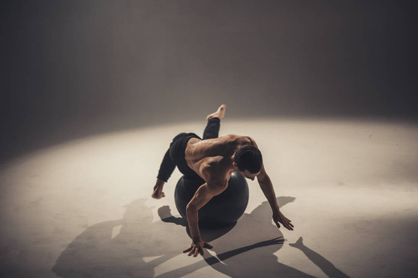 young man dancer making exercises and posing with yoga ball in studio - Foto, imagen
